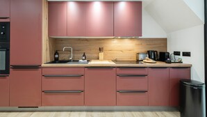 A modern kitchen with pink cabinets, a wooden backsplash, and a stainless steel sink. - Suite Cucumelle - Beau Duplex pour 6 avec balcon (Saint-Chaffrey)