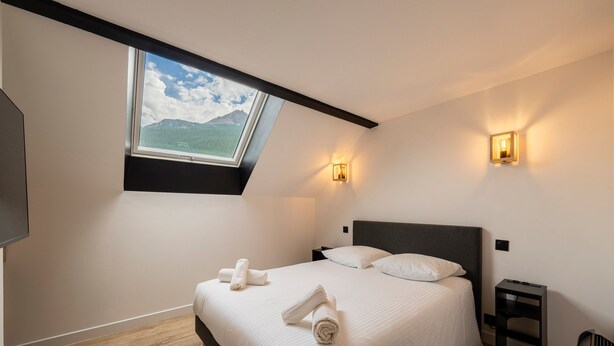 A bedroom with a skylight, a bed with pillows, a bedside table, and a nightstand. - Suite Cucumelle - Beau Duplex pour 6 avec balcon (Saint-Chaffrey)