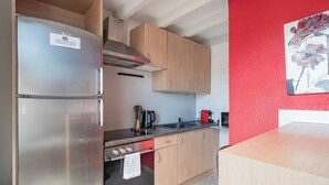 A modern kitchen with stainless steel appliances, wooden cabinets, and a red accent wall. - La Réserve de Fathala - À 500 m de la gare (Sarrebourg)
