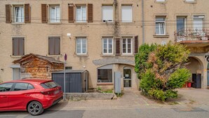 A red car parked in a driveway, a building with multiple windows and shutters, and a small garden area with a tree. - La Réserve de Fathala - À 500 m de la gare (Sarrebourg)
