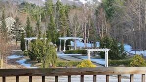 Um deck com almofadas vermelhas, uma pérgula e vista para uma paisagem nevada de montanhas.