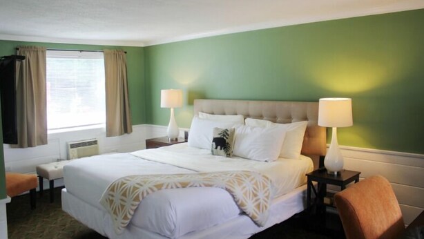 Quarto de hotel com uma cama, duas mesas de cabeceira, uma janela com cortinas e um abajur em cada mesa.