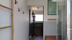 A hallway with a bamboo ladder, a wooden bench, a glass shower enclosure, and a framed poster on the wall. - Fargesia - Jolie maison avec jardin, proche plage (Fréhel)