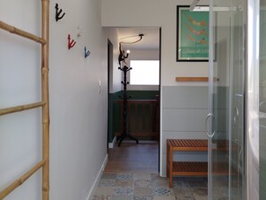 A hallway with a bamboo ladder, a wooden bench, a glass shower enclosure, and a framed poster on the wall. - Fargesia - Jolie maison avec jardin, proche plage (Fréhel)