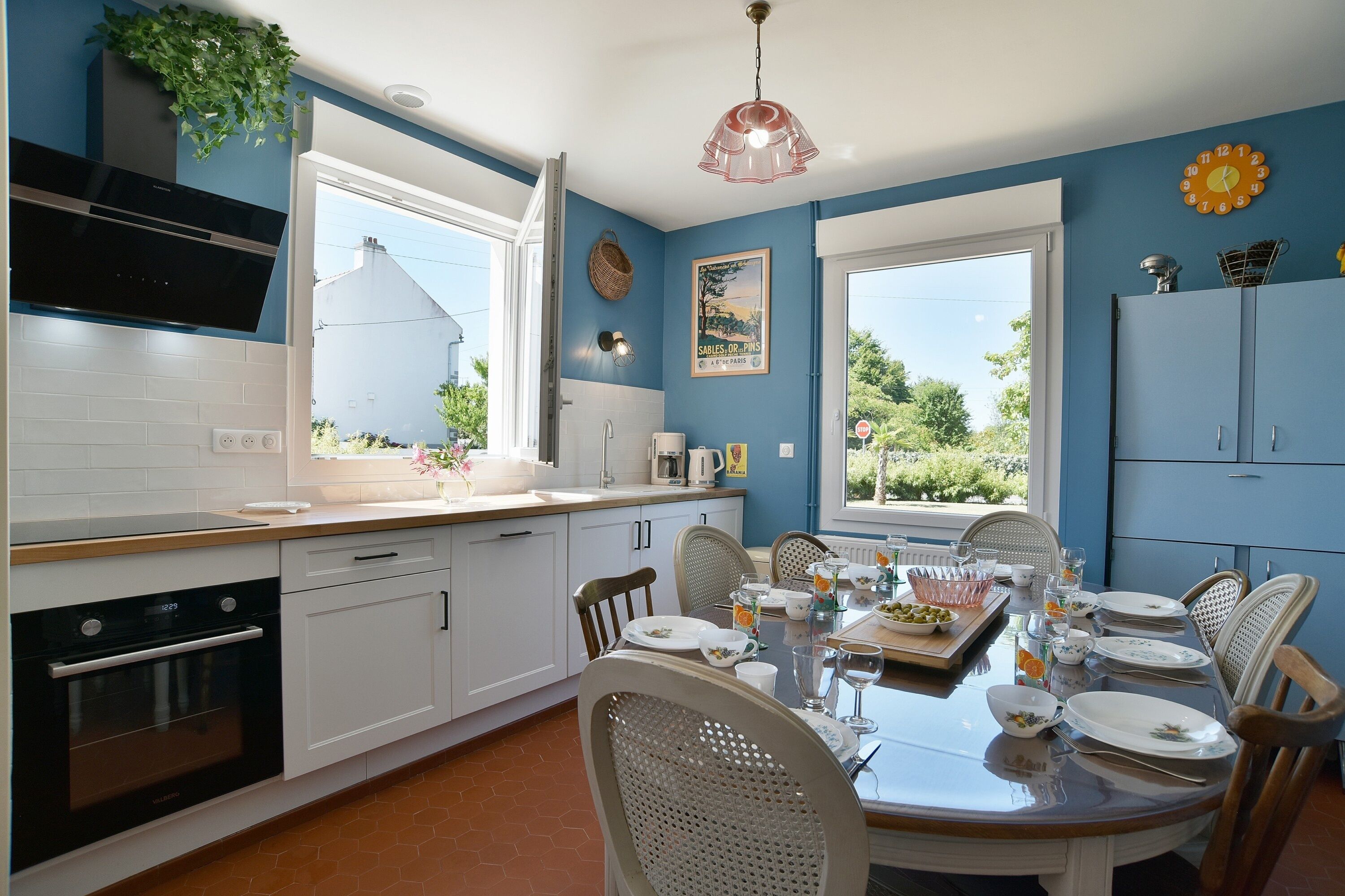 Una cocina moderna con armarios blancos, una mesa de comedor para seis personas y ventanas amplias que ofrecen luz natural.
