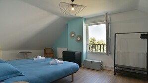 A bedroom with a large bed, a small table, a chair, a radiator, and a window with a view. - Fargesia - Jolie maison avec jardin, proche plage (Fréhel)