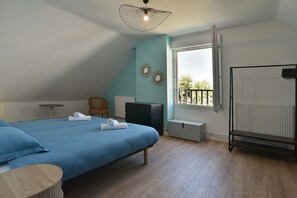 A bedroom with a large bed, a small table, a chair, a radiator, and a window with a view. - Fargesia - Jolie maison avec jardin, proche plage (Fréhel)