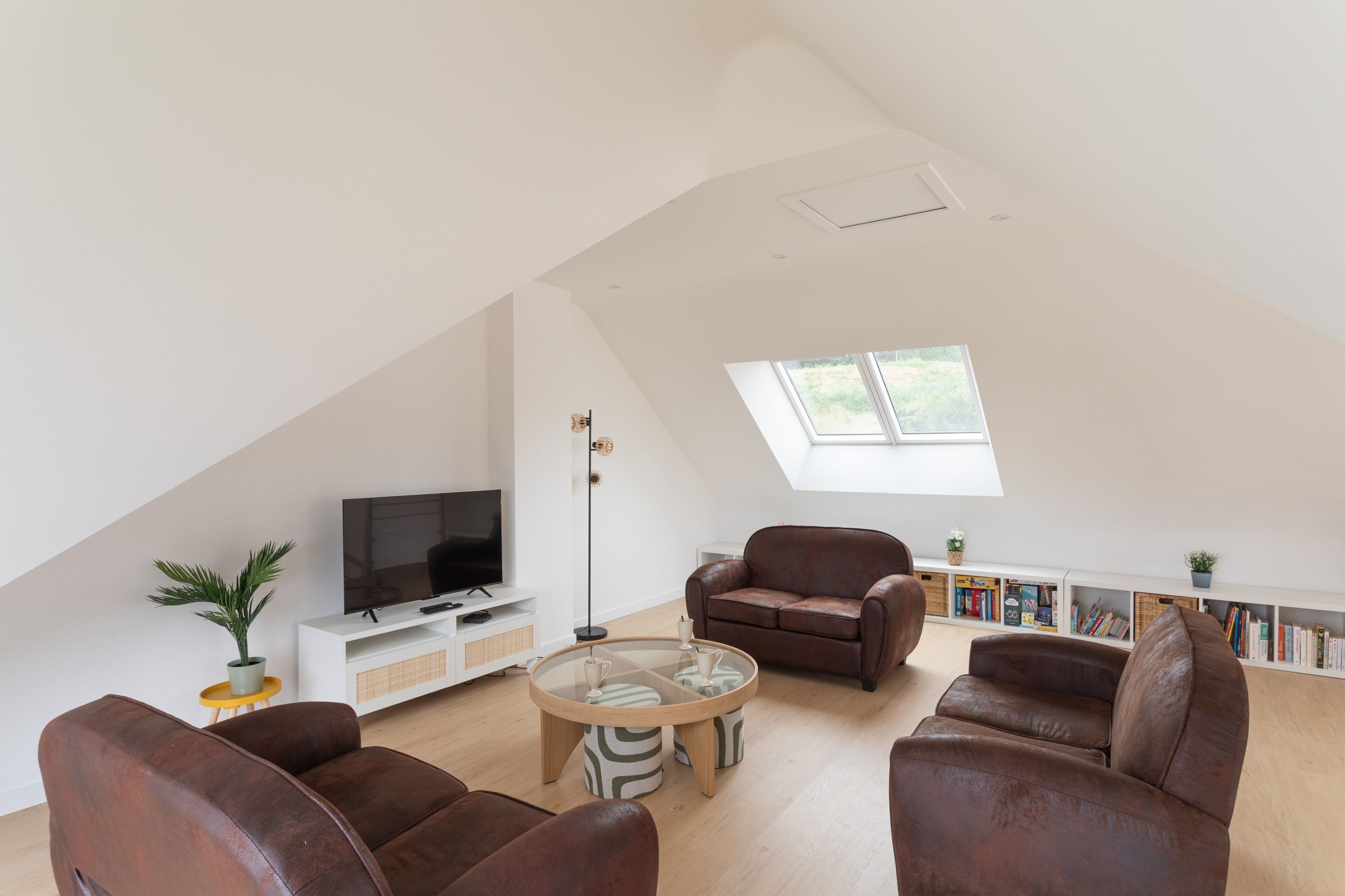 A spacious loft with a high ceiling, a large window, a flat-screen TV, leather sofas, a coffee table, and a bookshelf.
