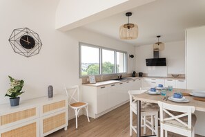 Eine moderne Küche mit weißen Schränken, einem großen Fenster und einer Essecke mit Tisch für zwei Personen.
