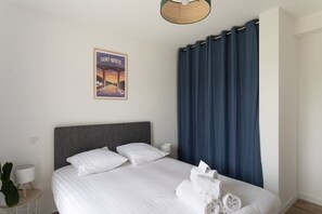 Ein ordentlich bezogenes Bett mit weißen Leinen, einem grauen Kopfteil und einem gerahmten Bild an der Wand.