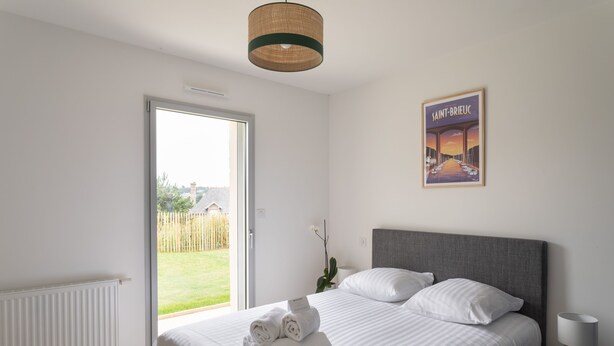 A bedroom with a bed, a window, a door, a wall-mounted lamp, and a poster. - Les horizons - À moins d'1 km de la plage (Erquy)