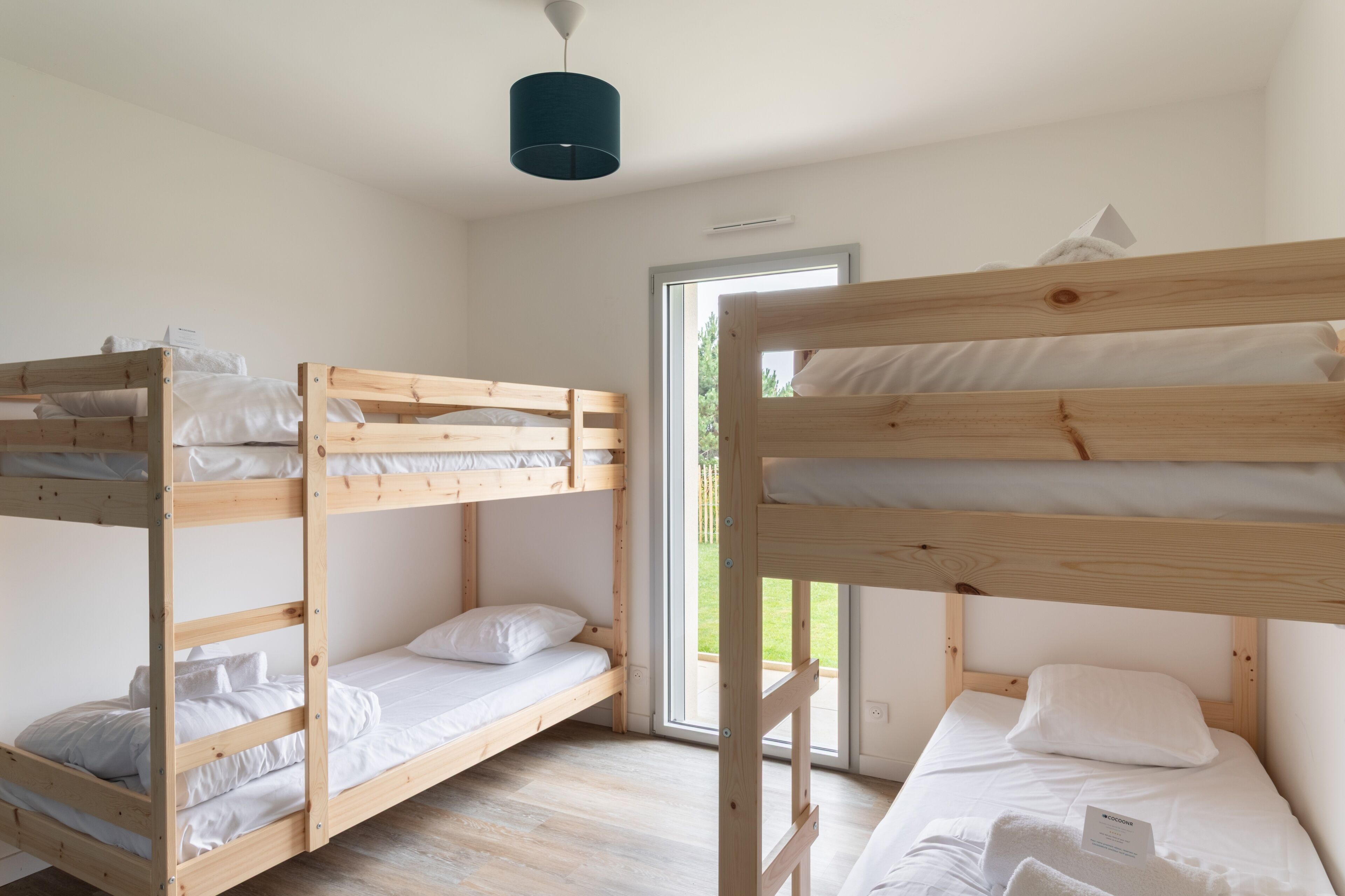 Une chambre avec un lit superposé, une structure en bois, du linge de lit blanc et un luminaire au plafond.