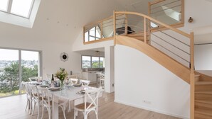 A spacious dining area with a high ceiling and large windows, a wooden staircase, and a view of the city. - Les horizons - À moins d'1 km de la plage (Erquy)