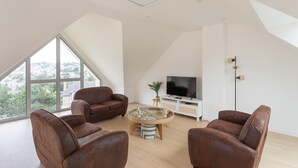 A modern living room with a large window, a flat-screen TV, and leather sofas. - Les horizons - À moins d'1 km de la plage (Erquy)