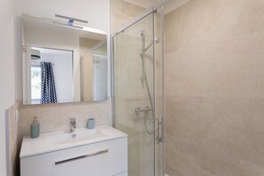 Et moderne badeværelse med en glasvæg omkring brusebadet, et hvidt møbel med spejl og en håndklædestang.