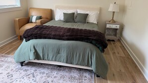 A bedroom with a bed, a chair, a nightstand, and a lamp. - Cozy 1-Bedroom Condo minutes from the Beach, Kill Devil Hills with AC (Kill Devil Hills)