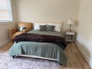 A bedroom with a bed, a chair, a nightstand, and a lamp. - Cozy 1-Bedroom Condo minutes from the Beach, Kill Devil Hills with AC (Kill Devil Hills)