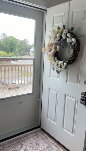 Una puerta blanca con un adorno decorativo, vistas a una terraza de madera y un tapete estampado.