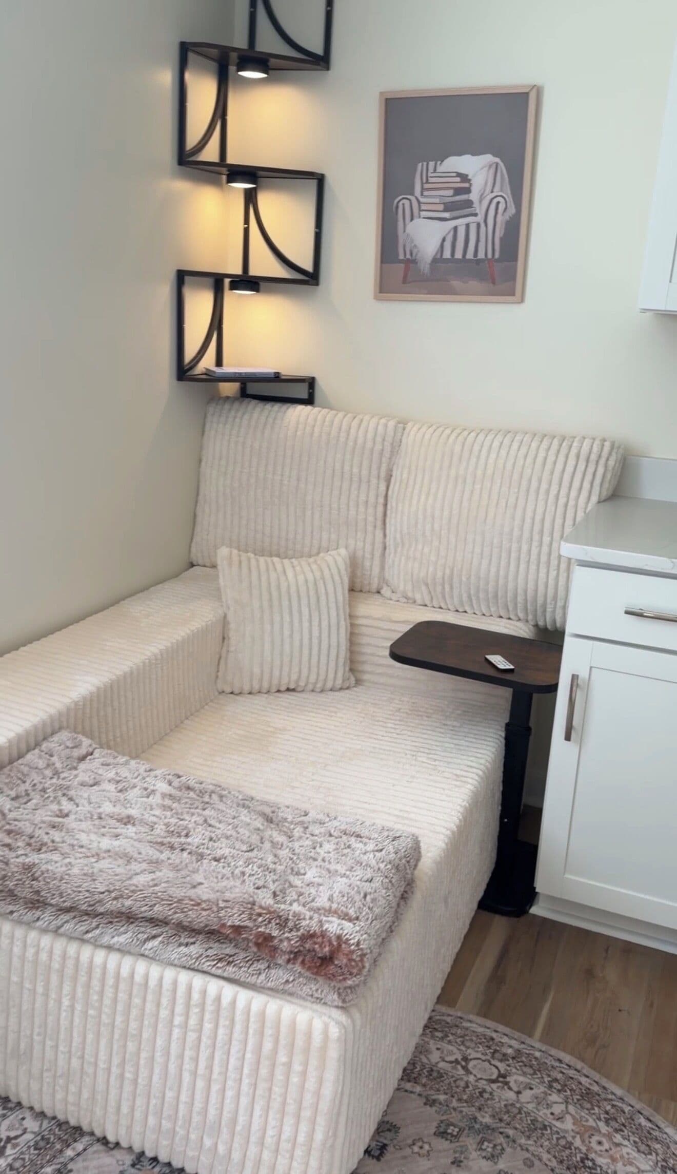 Un canapé d’angle avec un repose-pieds, une petite table, une télécommande et un tableau encadré au mur.