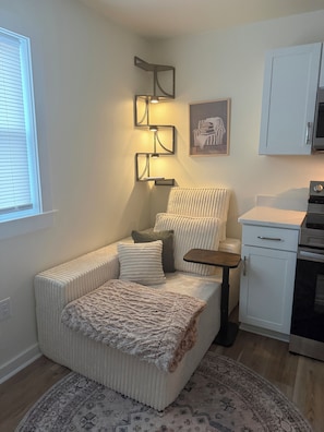 A compact living space with a sofa, a small table, a kitchen area, and a patterned rug. - Cozy 1-Bedroom Condo minutes from the Beach, Kill Devil Hills with AC (Kill Devil Hills)