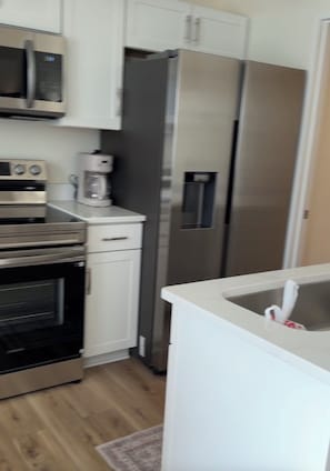 A kitchen with a microwave, oven, coffee maker, refrigerator, and a sink. - Cozy 1-Bedroom Condo minutes from the Beach, Kill Devil Hills with AC (Kill Devil Hills)