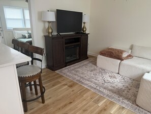 Ein Wohnzimmer mit Flachbildfernseher, zwei Lampen, einem Sofa, einem Sessel und einem gemusterten Teppich.