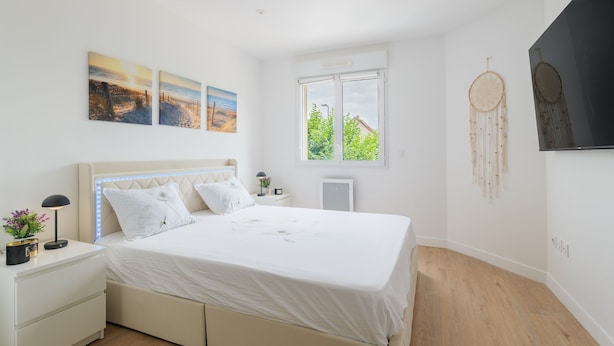 Ein Schlafzimmer mit einem Bett, Nachttischen, Wandbildern und einem großen Fenster.