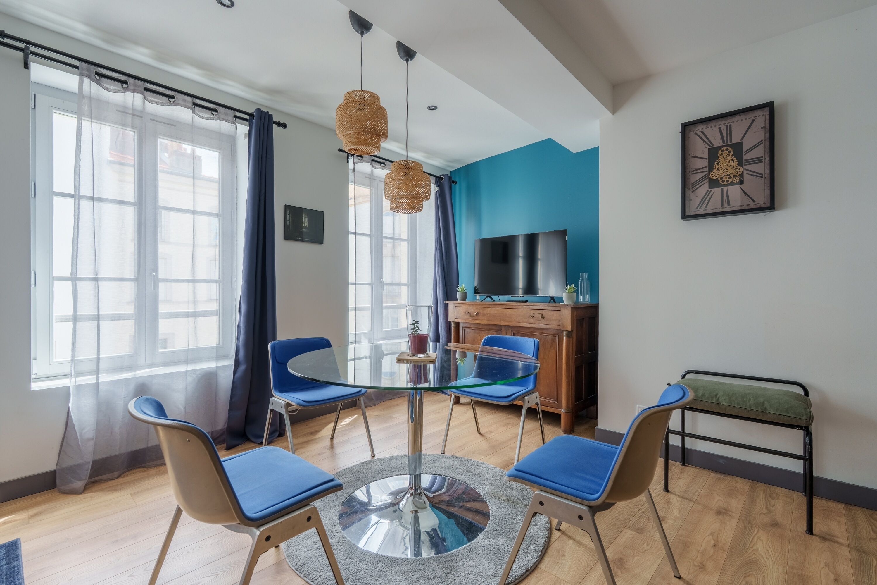 Een moderne kamer met een glazen tafel, blauwe stoelen, een televisie en een blauwe accentmuur.