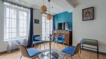 Een moderne kamer met een glazen tafel, blauwe stoelen, een televisie en een blauwe accentmuur.