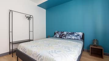 Een slaapkamer met een bed, een metalen kledingkast, een nachtkastje en een blauwe accentmuur.