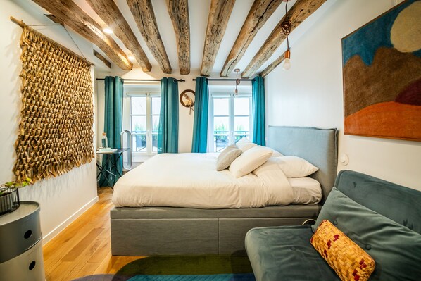 A modern bedroom with a large bed, a grey sofa, and a woven wall hanging. - Marais Colors - À 750 m de la place de la Bastille (Paris)