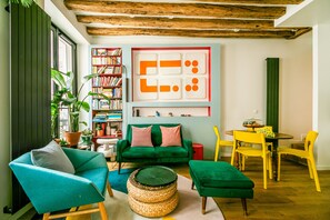 A cozy living room with a green sofa, teal armchair, and yellow chairs. There's a bookshelf filled with books and a decorative wall piece. - Marais Colors - À 750 m de la place de la Bastille (Paris)