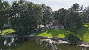 Ein Haus mit einem Steg, der sich über das Wasser erstreckt, umgeben von Bäumen und einer Wiese.