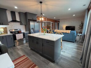 A modern kitchen with dark cabinets, a central island, and a hanging light fixture.