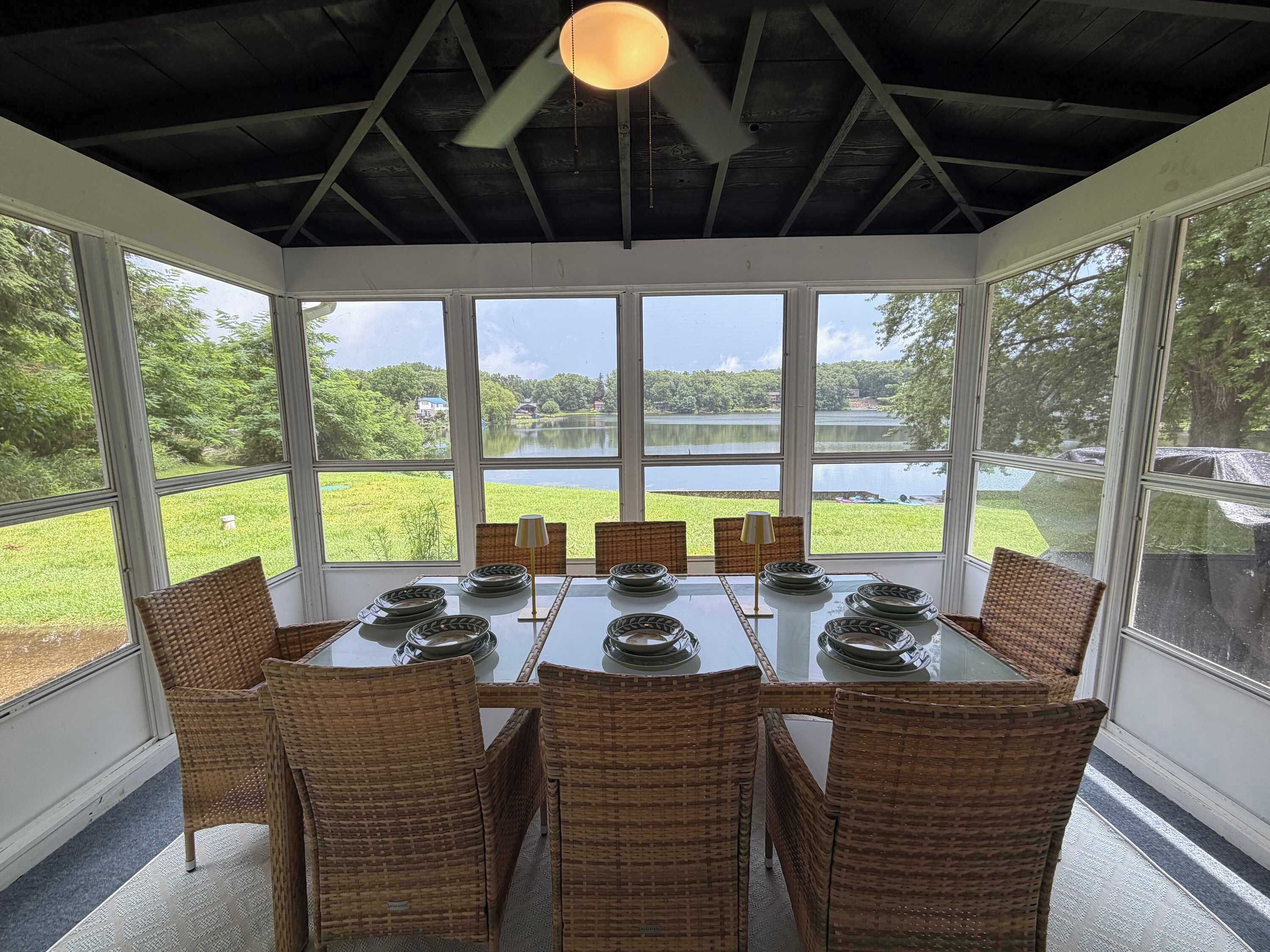 A conservatory with a table set for six, wicker chairs, and a view of a lake.