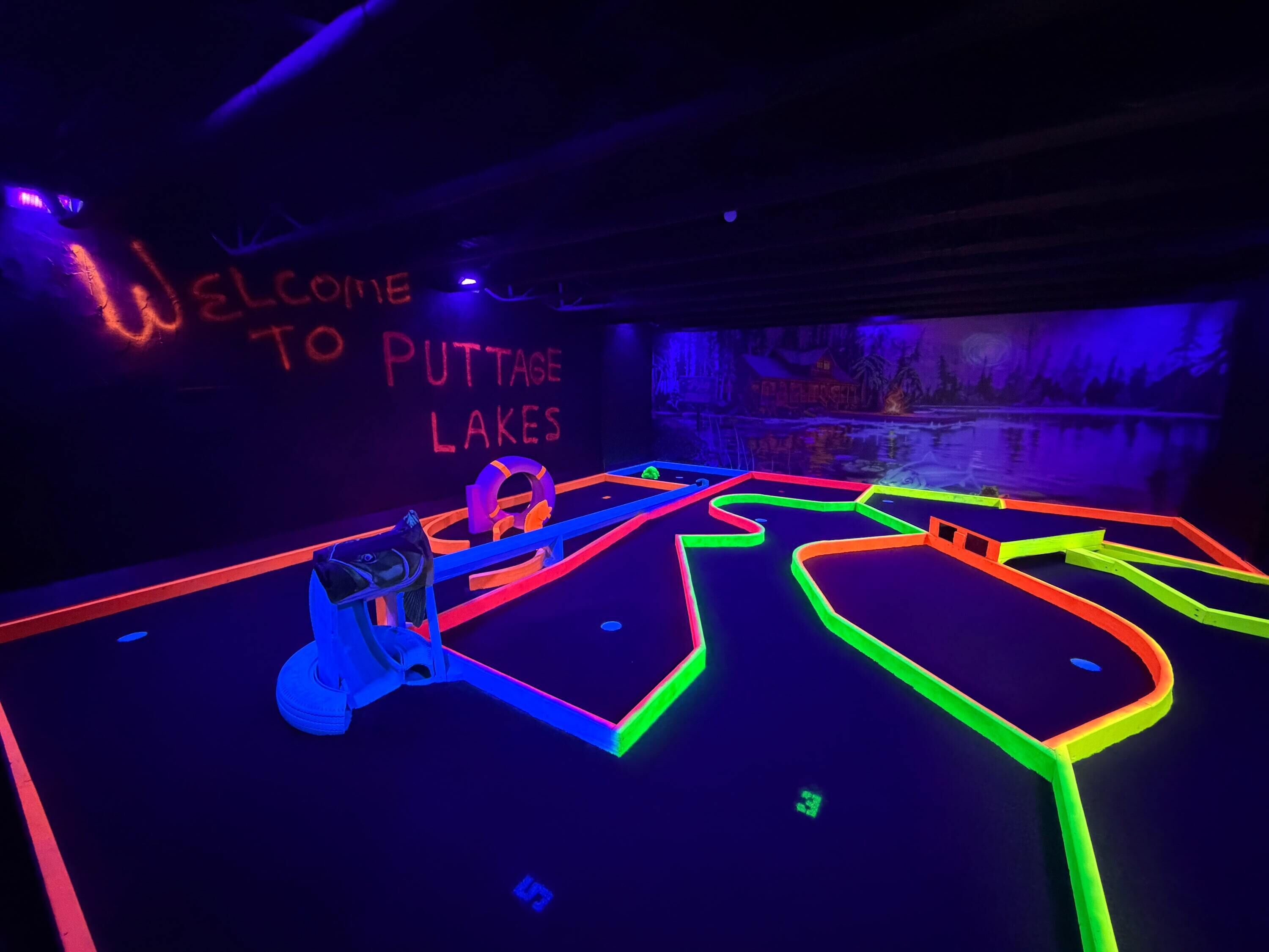 An indoor neon-lit maze with a sign reading 'Welcome to Puttaway Lakes.'