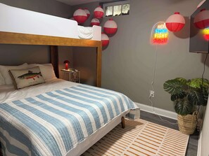 Ein Schlafzimmer mit Etagenbett, Nachttischlampe, einer Neonreklame und einem Blumentopf.