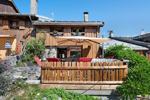 Una cabaña de madera con terraza, mobiliario exterior y chimenea de piedra.