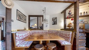 Un comedor rústico con una mesa de madera y bancos, una lámpara colgante y una pared de madera con estantes.