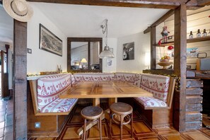 Ein rustikaler Essbereich mit Holztisch und Bänken, einer hängenden Leuchte und einer Holzwand mit Regalen.
