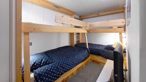 Habitación con literas, un escritorio, una silla, un estante pequeño y una ventana.