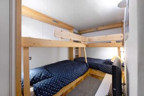 Ein Schlafsaal mit Etagenbetten, einem Schreibtisch, einem Stuhl, einem kleinen Regal und einem Fenster.