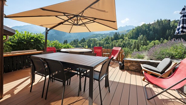 Una terraza al aire libre con una mesa, sillas, un paraguas grande y una vista panorámica de la montaña.