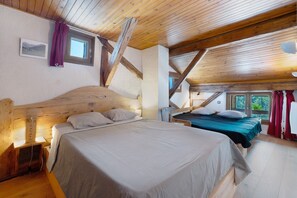 Un dormitorio con una cama grande, una cama más pequeña, vigas de madera, una ventana y vistas al follaje.