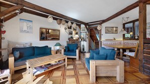 Un salón acogedor con vigas de madera, sofás azules, una mesa de centro de madera y una escalera que sube a otro nivel.