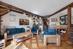 Ein gemütliches Wohnzimmer mit Holzbalken, blauen Sofas, einem Holztisch und einer Treppe, die zu einer anderen Ebene führt.