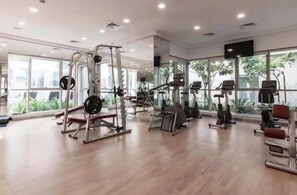 Ein geräumiges Fitnessstudio mit verschiedenen Trainingsgeräten, großen Fenstern und ebenem Boden.