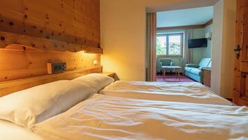 A hotel room with a wooden headboard, a bed with white linens, a television mounted on the wall, and a view of the outside through a window.