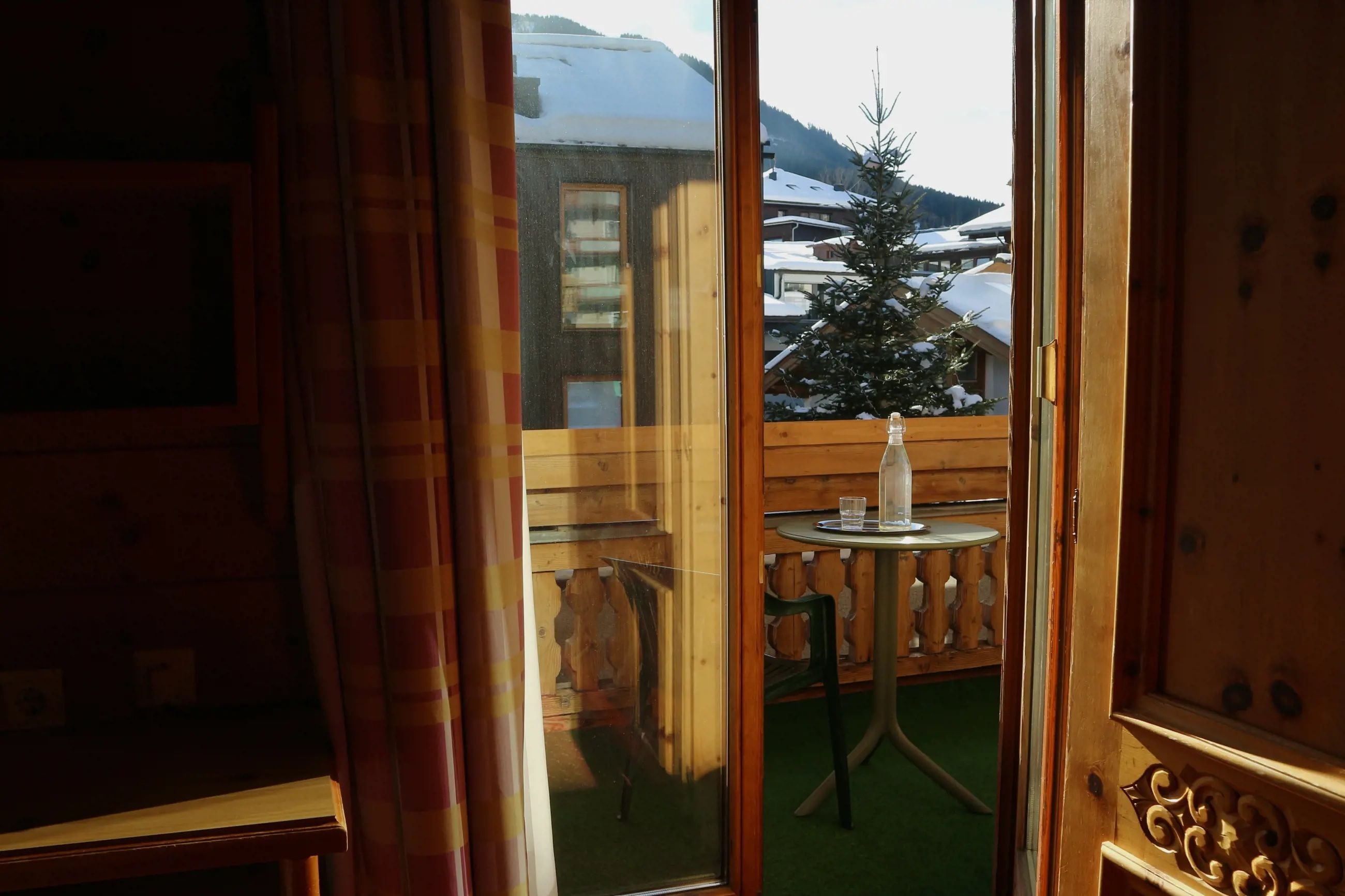 Una cabaña de madera con balcón, una mesa con un vaso y un paisaje cubierto de nieve.
