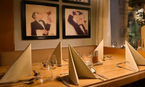 Un tavolo imbandito con menu, bicchieri e posate, con un'opera d'arte incorniciata sulla parete alle spalle.